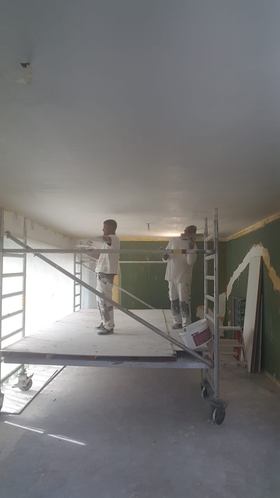 Twee vakmensen werken op steiger aan wanden en plafond